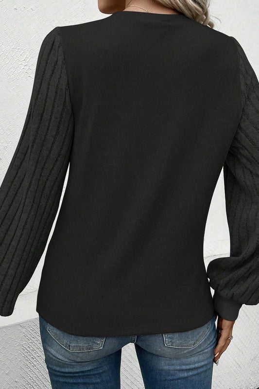 Black long-sleeve top worn by a person against a white wall