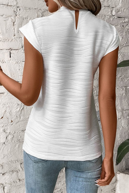 Person wearing a white patterned top and blue jeans against a textured wall.