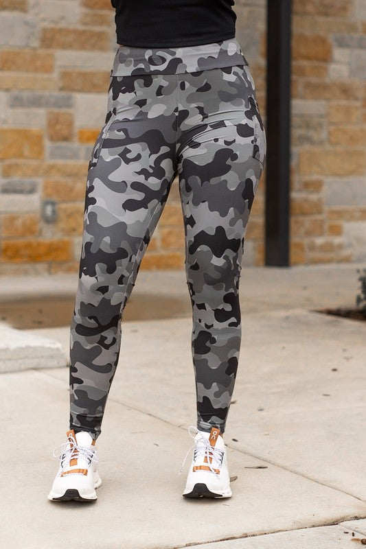 Person wearing camouflage leggings and white sneakers on a sidewalk.