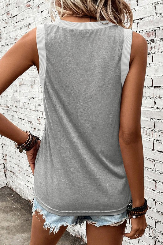 Person wearing a gray sleeveless top and denim shorts against a white brick wall.