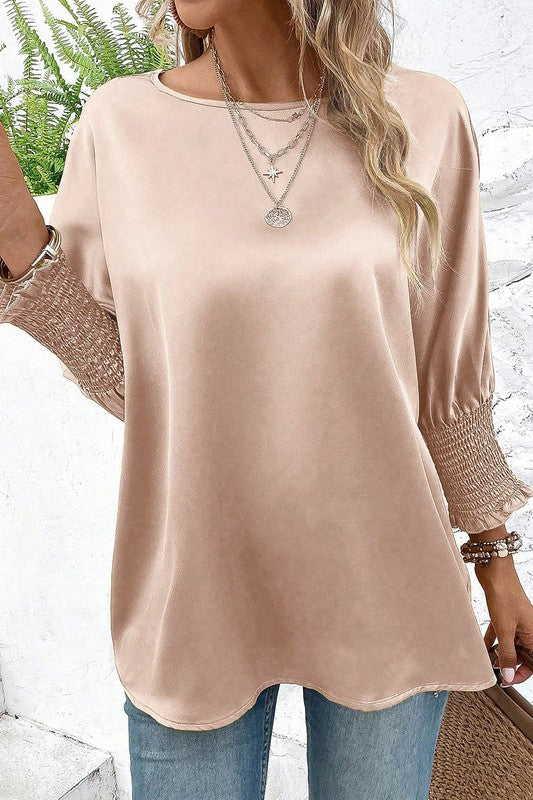 Woman wearing a beige long-sleeve top with lace cuffs against a white background