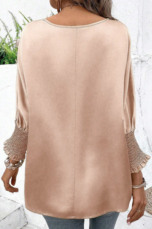 Beige blouse with lace cuffs worn by a person, against a white wall.