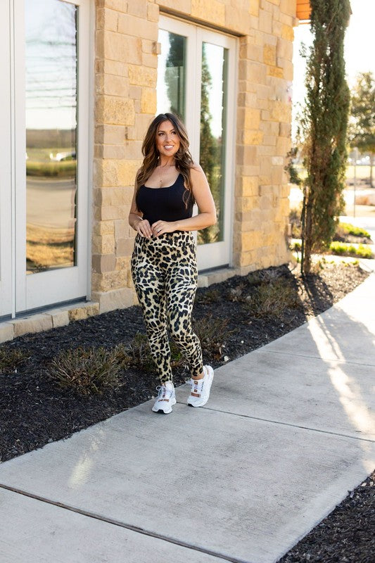 Woman in leopard print pants and black top standing on a sidewalk in front of a building.