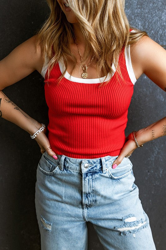 Person wearing a red tank top and blue jeans against a dark background
