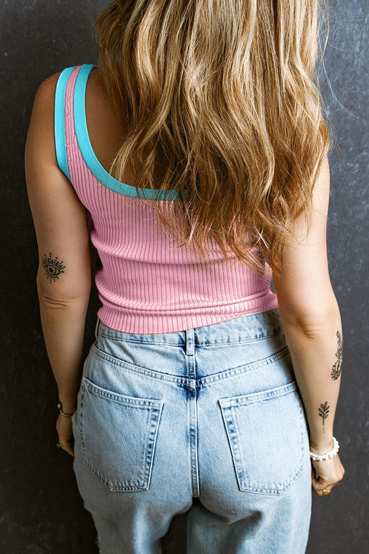 Person wearing a pink tank top with teal straps and blue jeans against a dark background