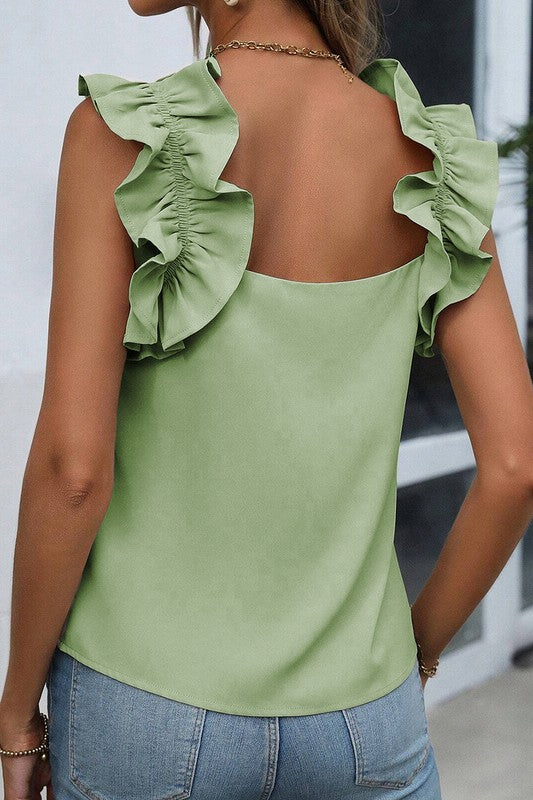 Green top with ruffled shoulders worn by a person, blurred background