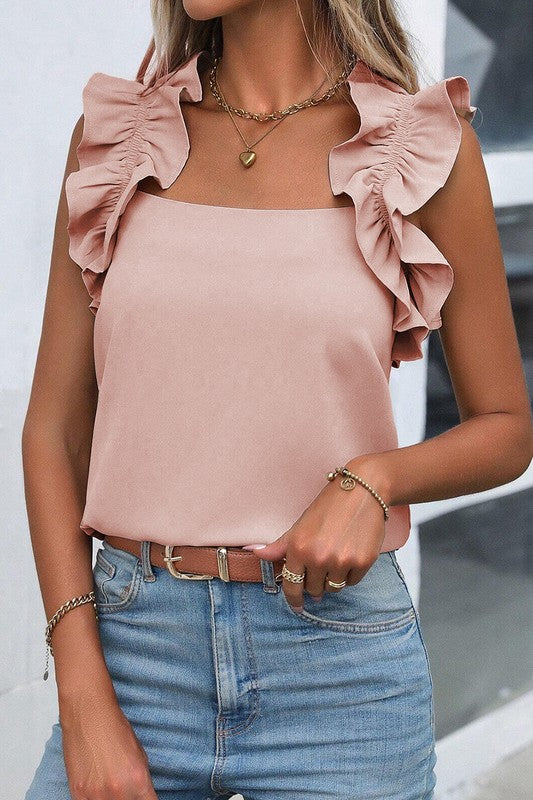 Woman wearing a pink top with ruffled shoulders and blue jeans.