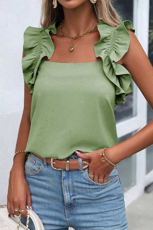 Woman wearing a green top with ruffled sleeves and blue jeans.
