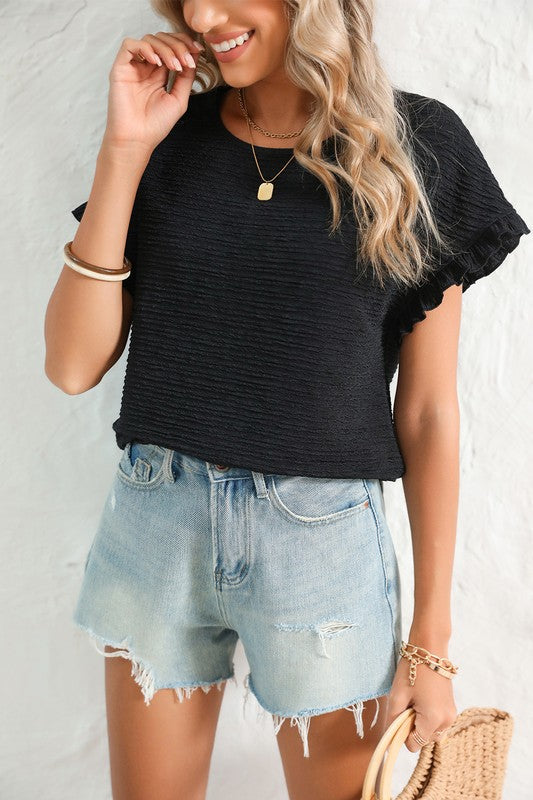 Woman wearing a black top and denim shorts against a white background