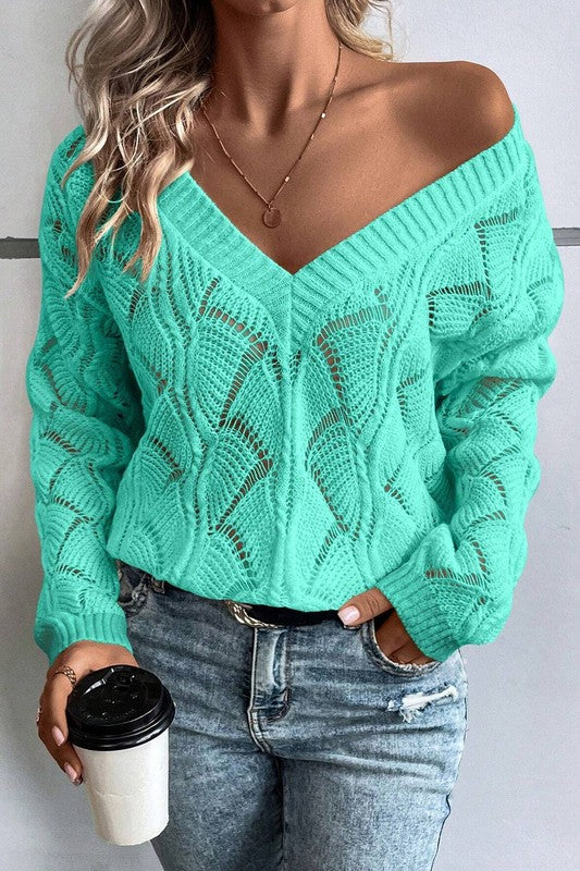 Person wearing a green off-shoulder sweater and blue jeans, holding a coffee cup.