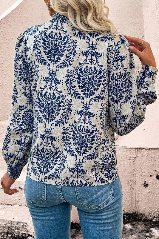 Person wearing a blue and white patterned blouse with blue jeans against a textured wall.