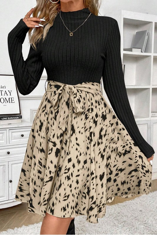 Person wearing a black ribbed long-sleeve top and a beige leopard print skirt in a room.