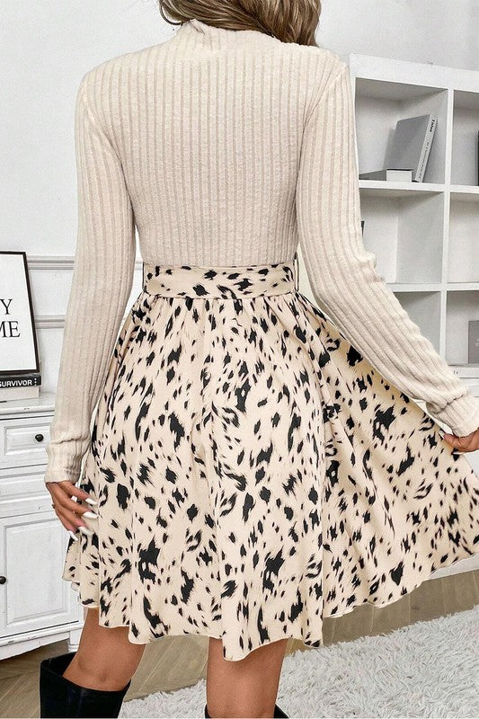 Person wearing a beige ribbed sweater and patterned skirt in a room with white shelves.