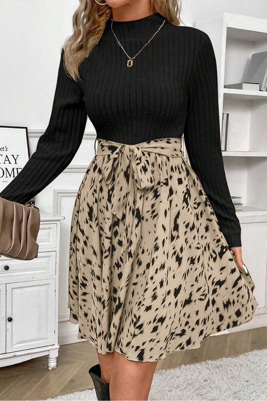 Woman wearing a black long-sleeve top and leopard print skirt in a room with white shelves.