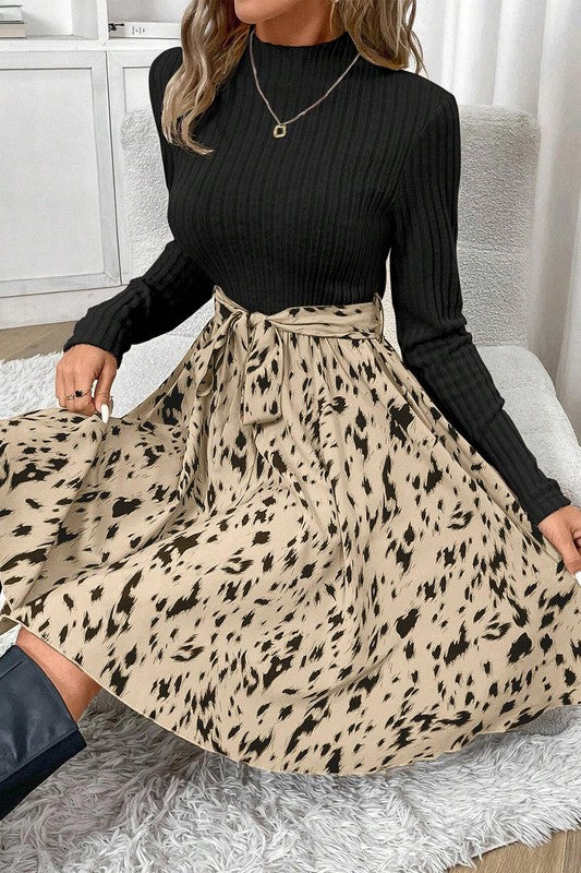 Woman wearing a black long-sleeve top and beige leopard print skirt sitting on a couch.