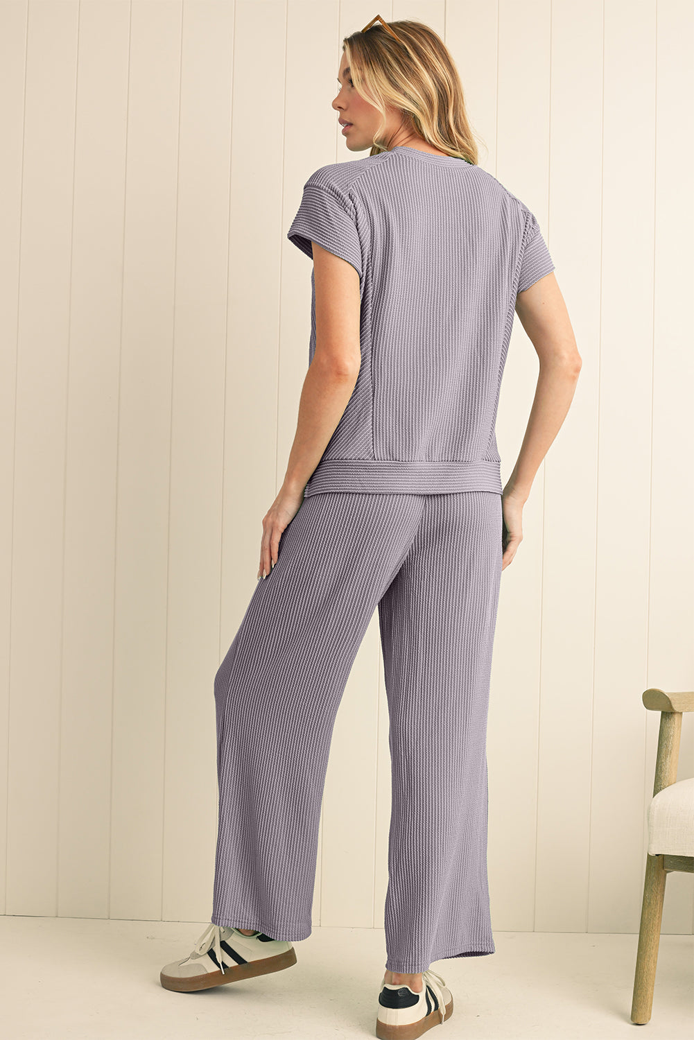 Woman wearing a light purple outfit with a matching top and pants against a white wall.