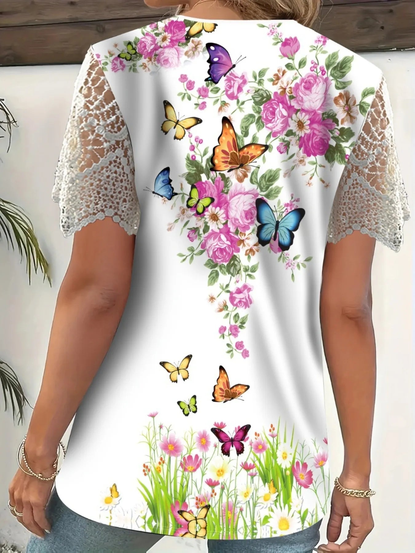 Woman wearing a floral and butterfly printed top with lace sleeves on a white background