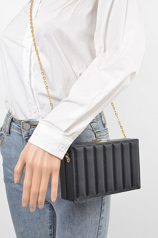 Person holding a black ribbed clutch bag with a gold chain strap on a white background