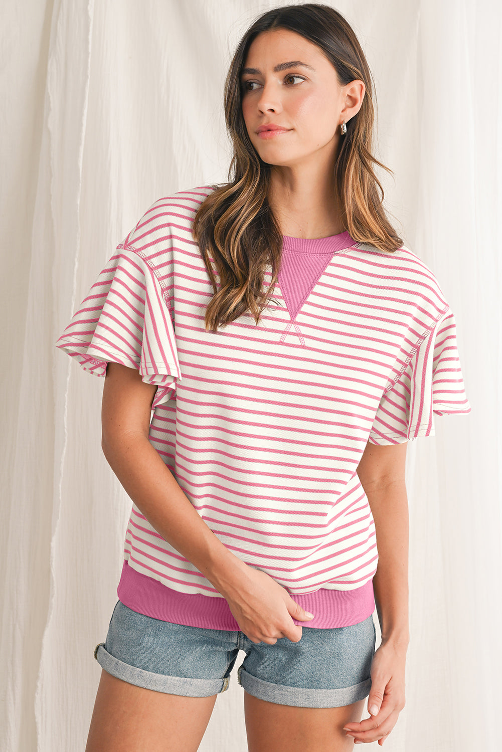 Woman wearing a pink and white striped shirt with a V-neck and denim shorts against a white background