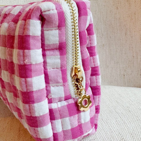 Pink and white checkered pouch with a gold zipper on a beige background