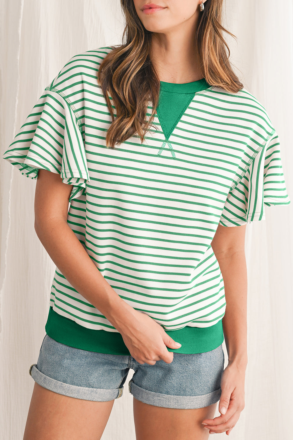 Woman wearing a green and white striped shirt with denim shorts against a white background