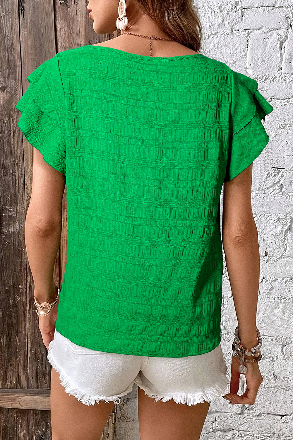Person wearing a green textured top and white shorts against a wooden and white brick wall.