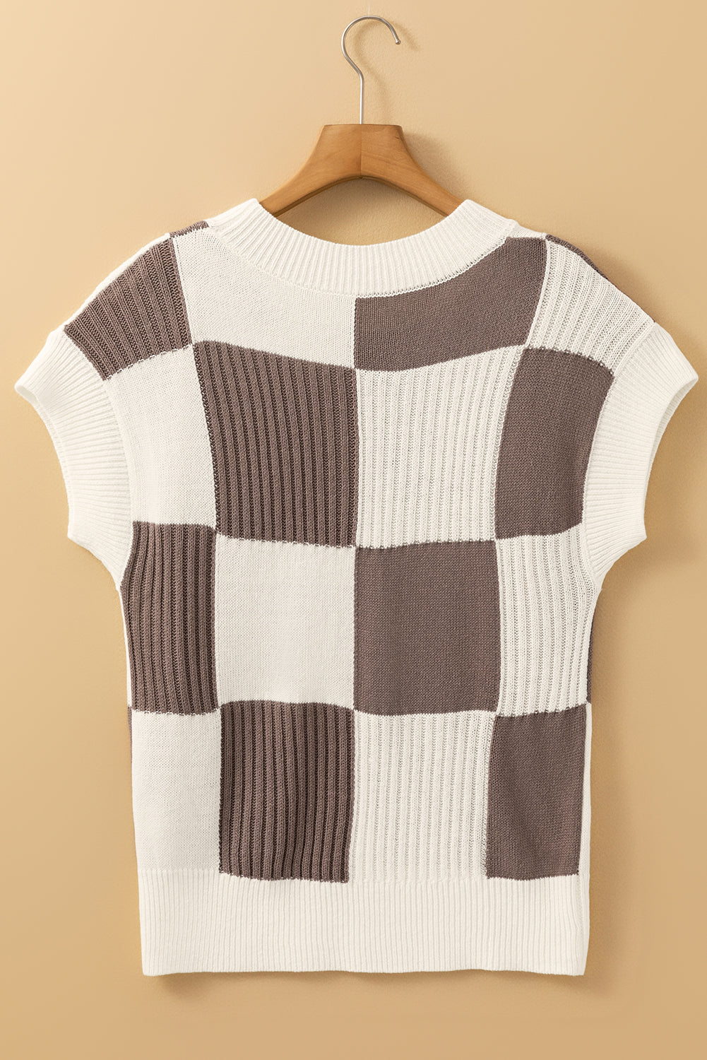 Checkered patterned sweater on a wooden hanger against a beige background