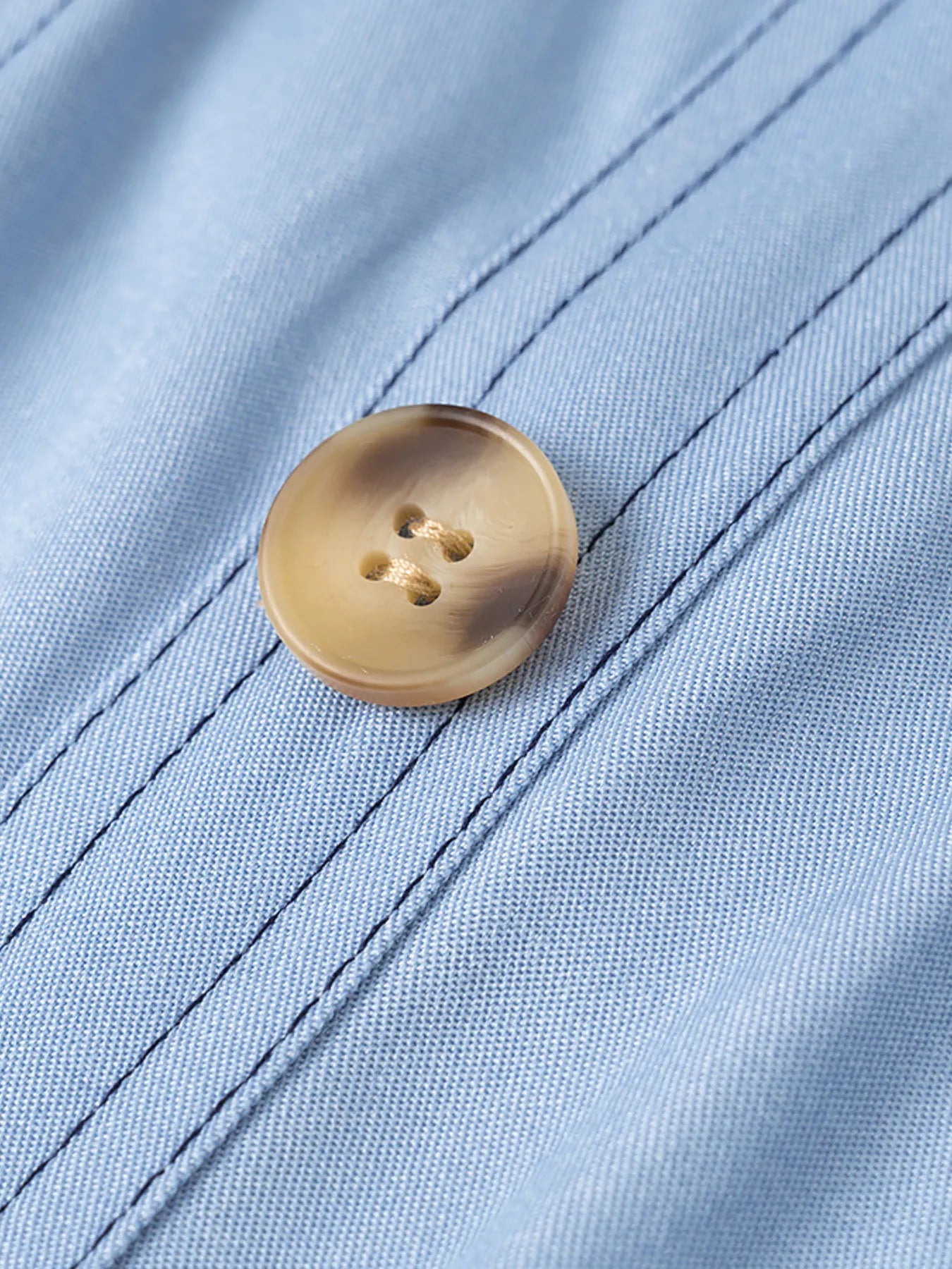 Close-up of a gold button on light blue fabric