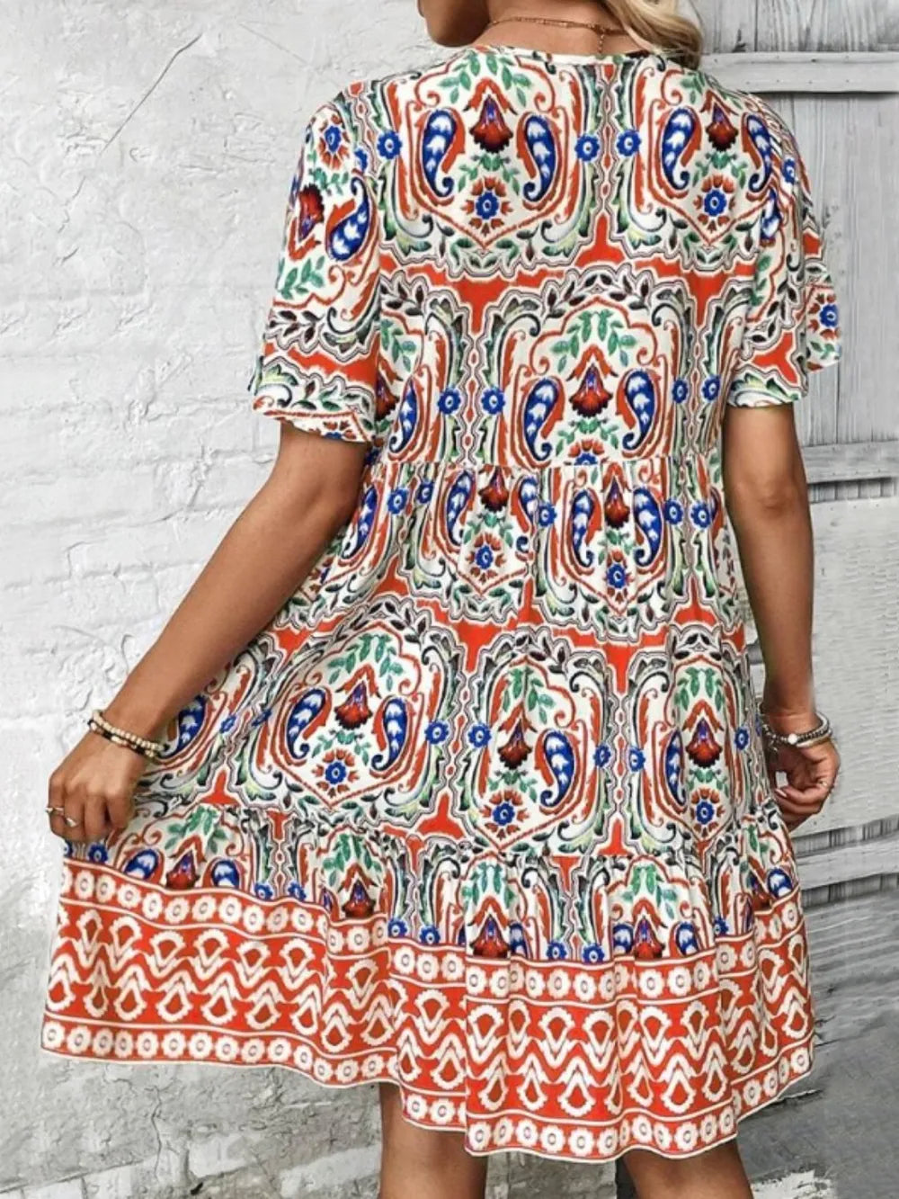 Woman wearing a colorful patterned dress against a white brick wall.