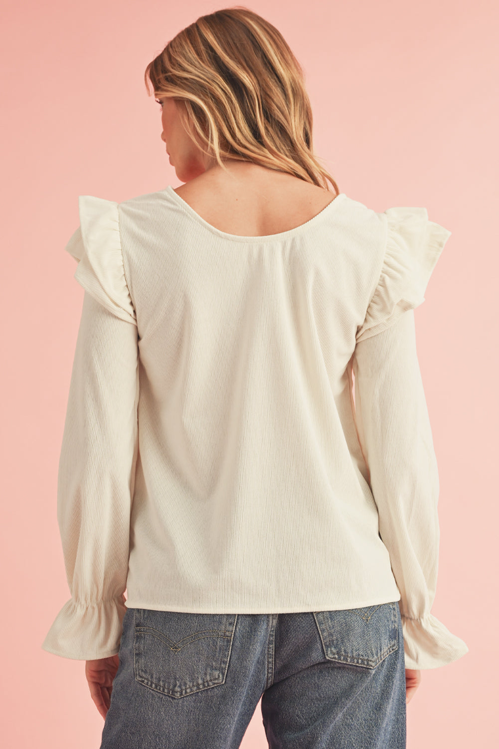 Woman wearing a cream blouse with ruffled sleeves on a pink background
