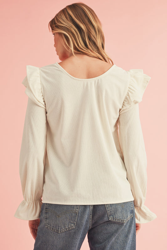 Woman wearing a cream blouse with ruffled sleeves on a pink background