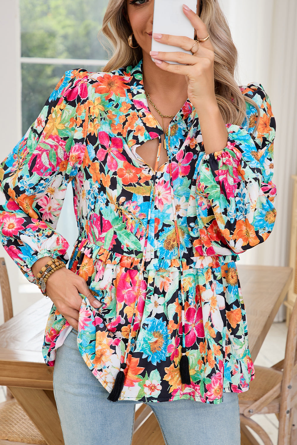 Woman wearing a colorful floral blouse sitting on a chair indoors.