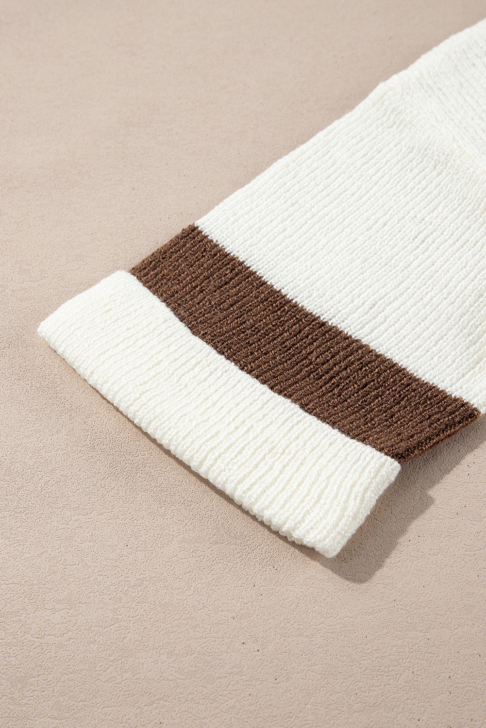 Close-up of a knitted blanket with white and brown stripes on a beige background