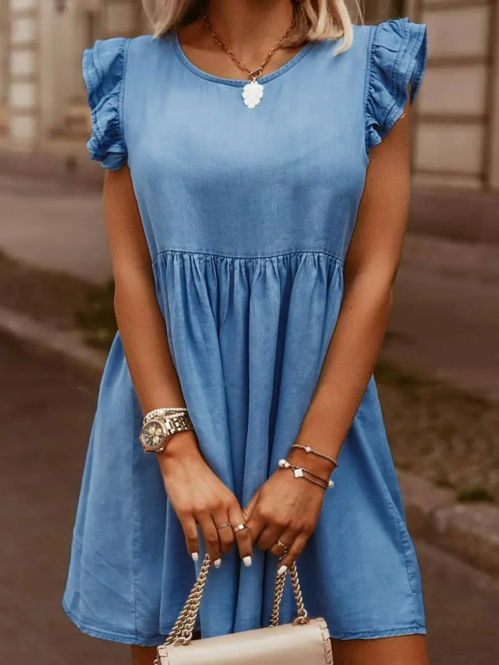 Woman wearing a blue dress holding a beige handbag with a blurred background