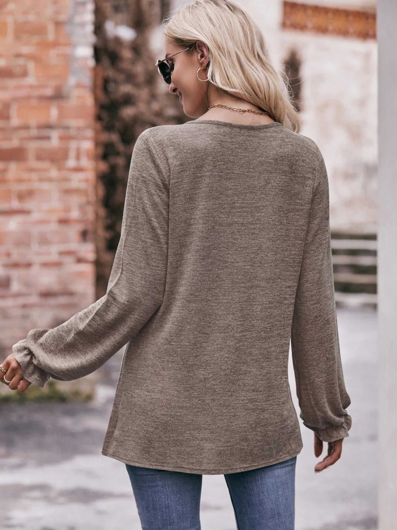 Woman wearing a long-sleeve brown top and blue jeans, standing outdoors.