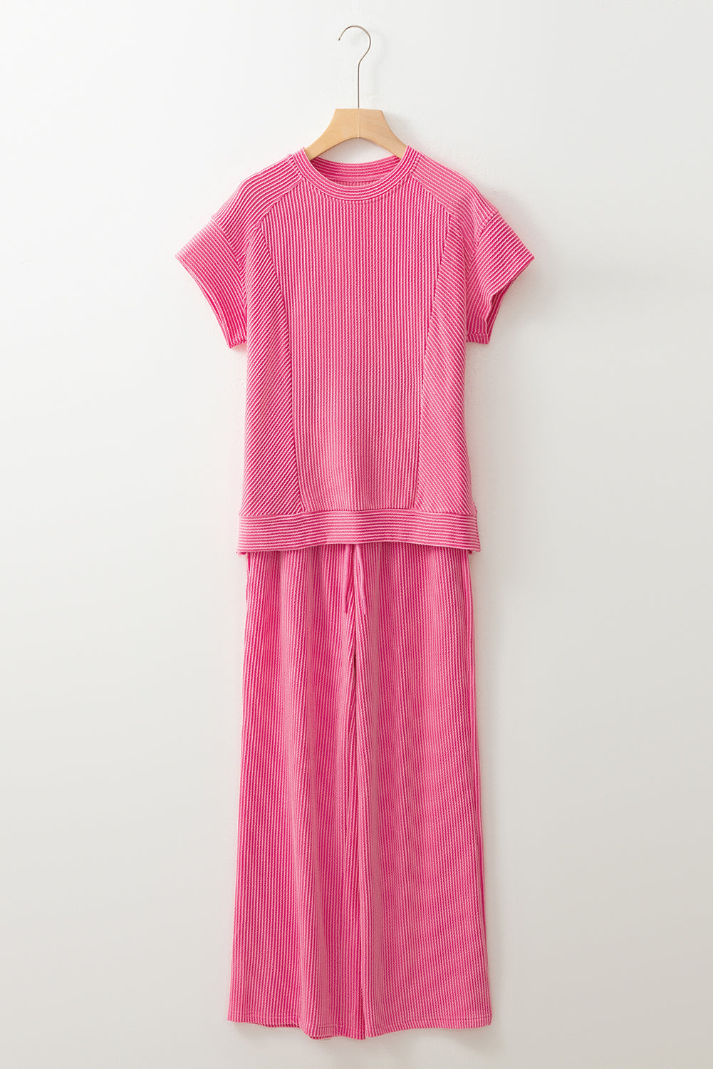 Pink outfit with a top and pants on a hanger against a white background