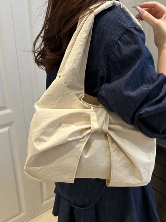 Person wearing a beige bag over one shoulder with a neutral background