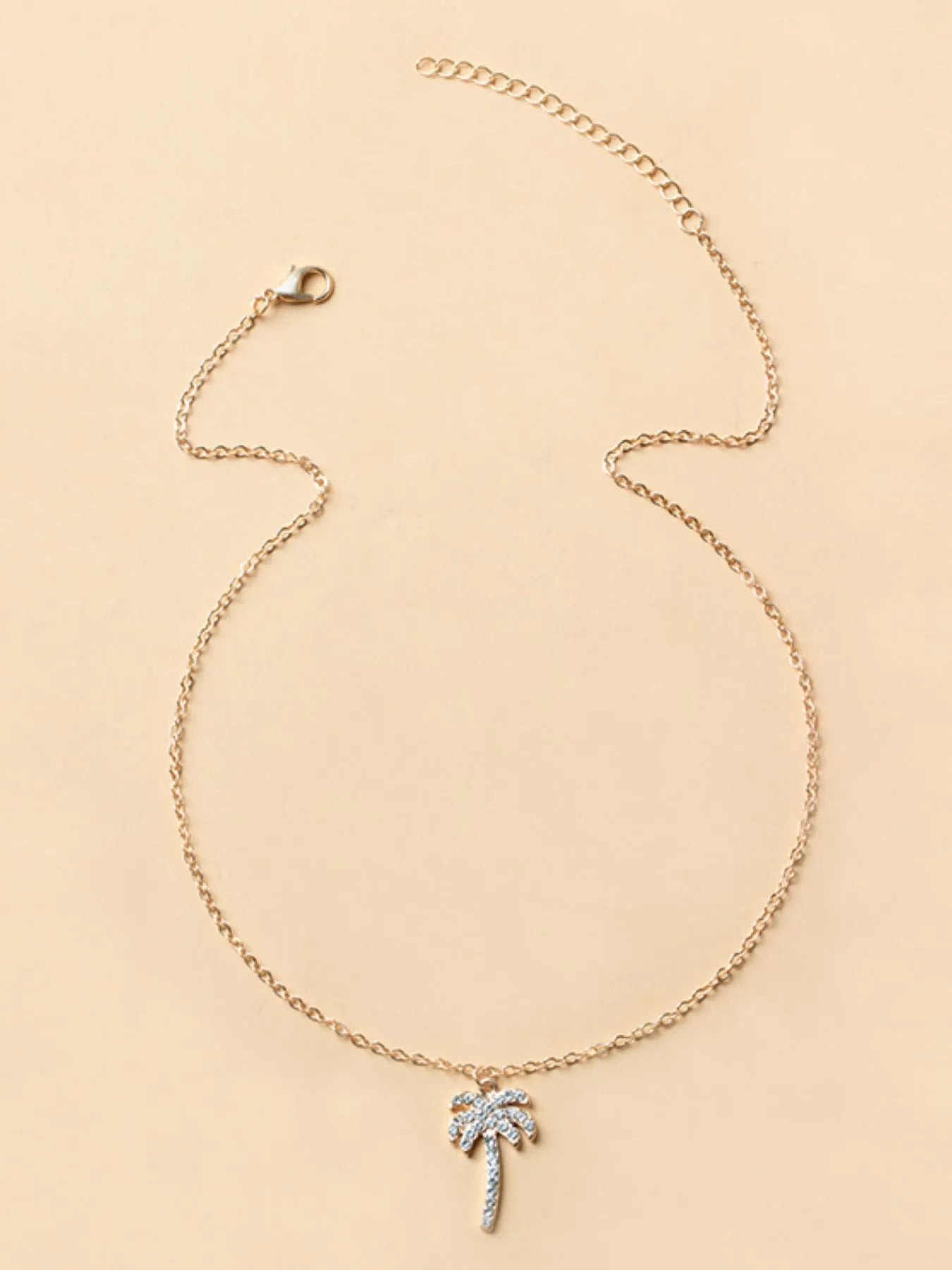 Gold necklace with a palm tree pendant on a beige background