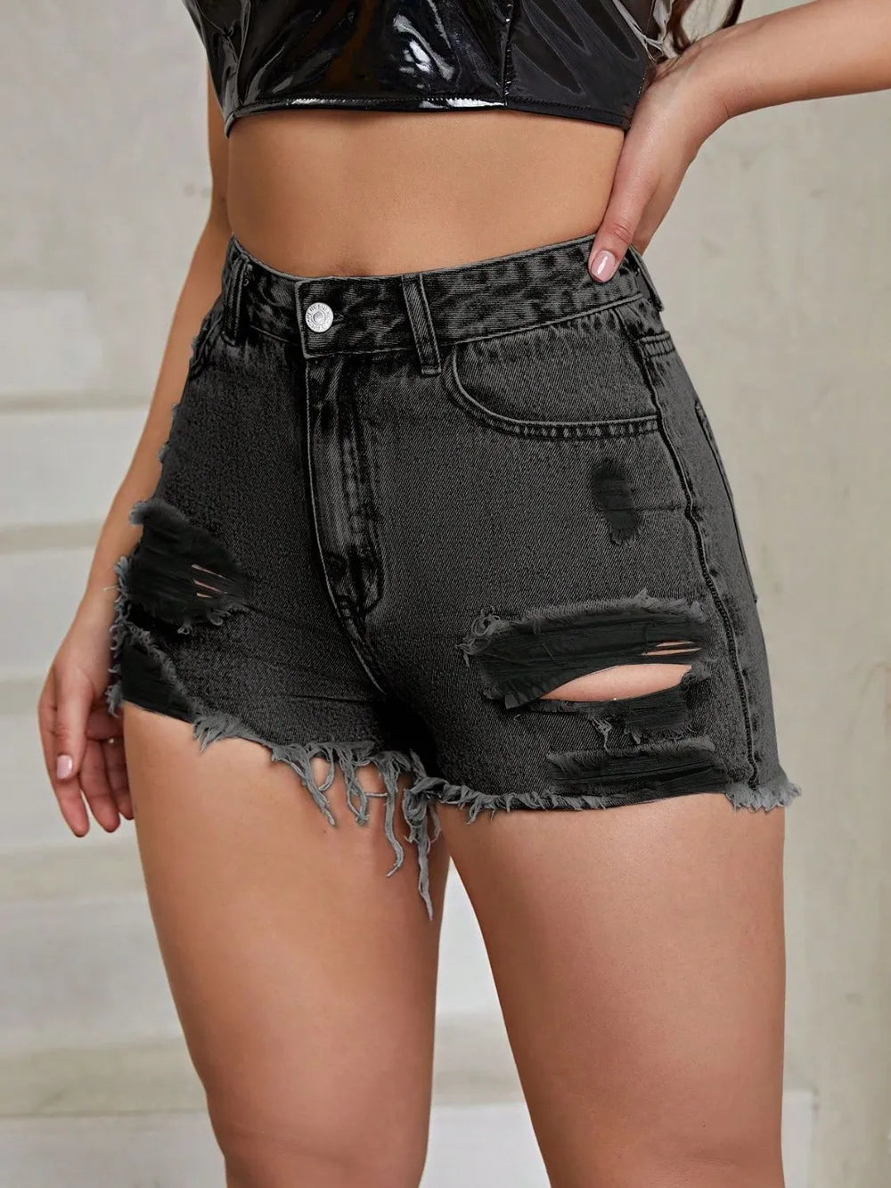 Black denim shorts with distressed details worn by a person against a neutral background