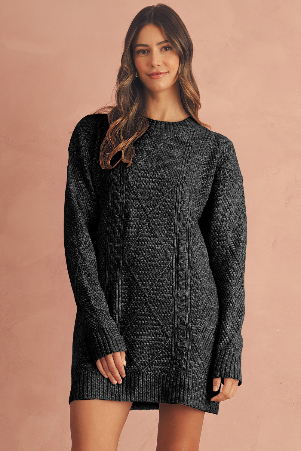Woman wearing a dark gray cable knit sweater dress against a pink background