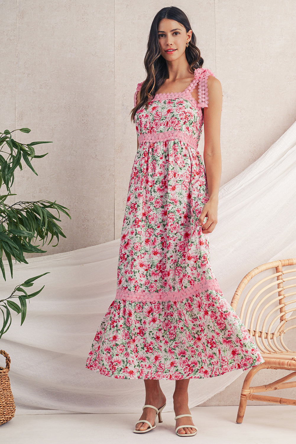 Woman wearing a floral dress standing in a minimalistic room with a plant and chair.