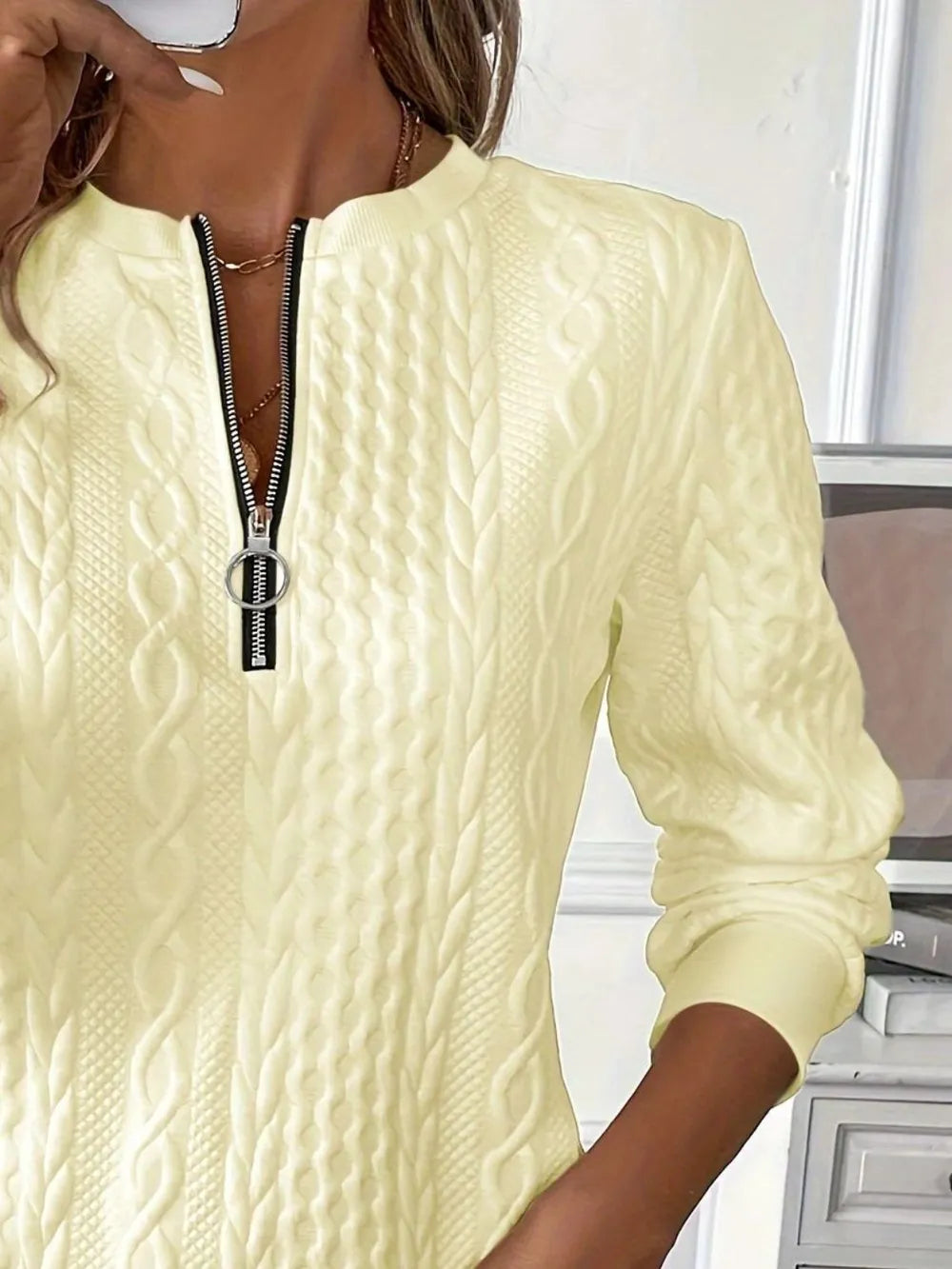Light yellow cable knit sweater with a zipper detail worn by a person indoors.