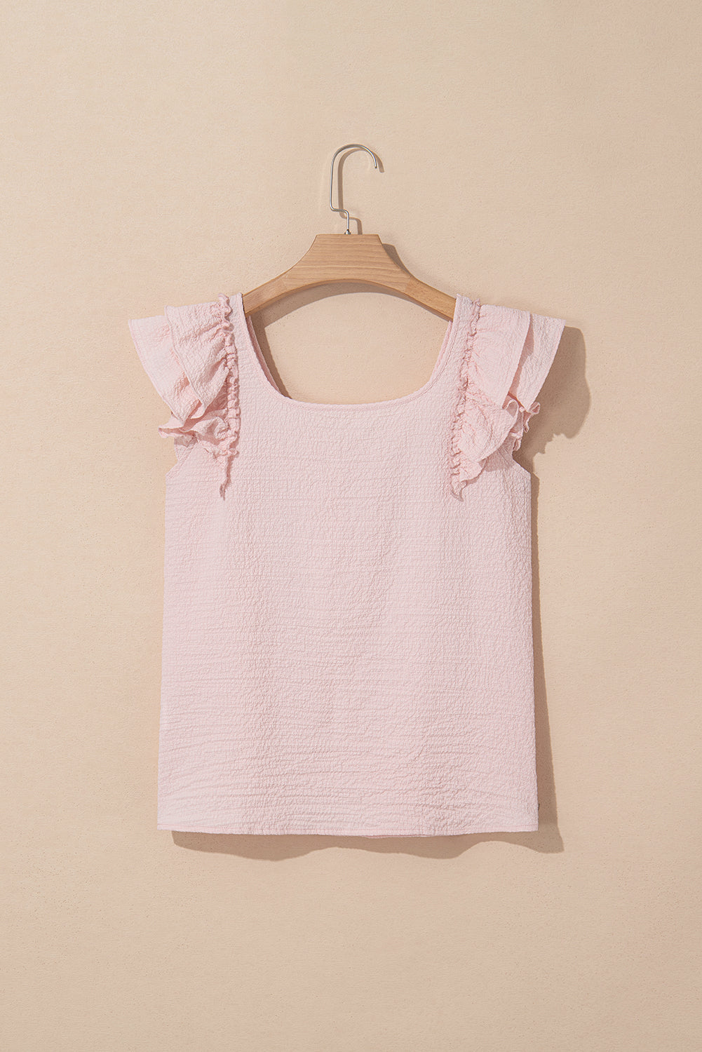 Pink sleeveless top with ruffled sleeves on a beige background