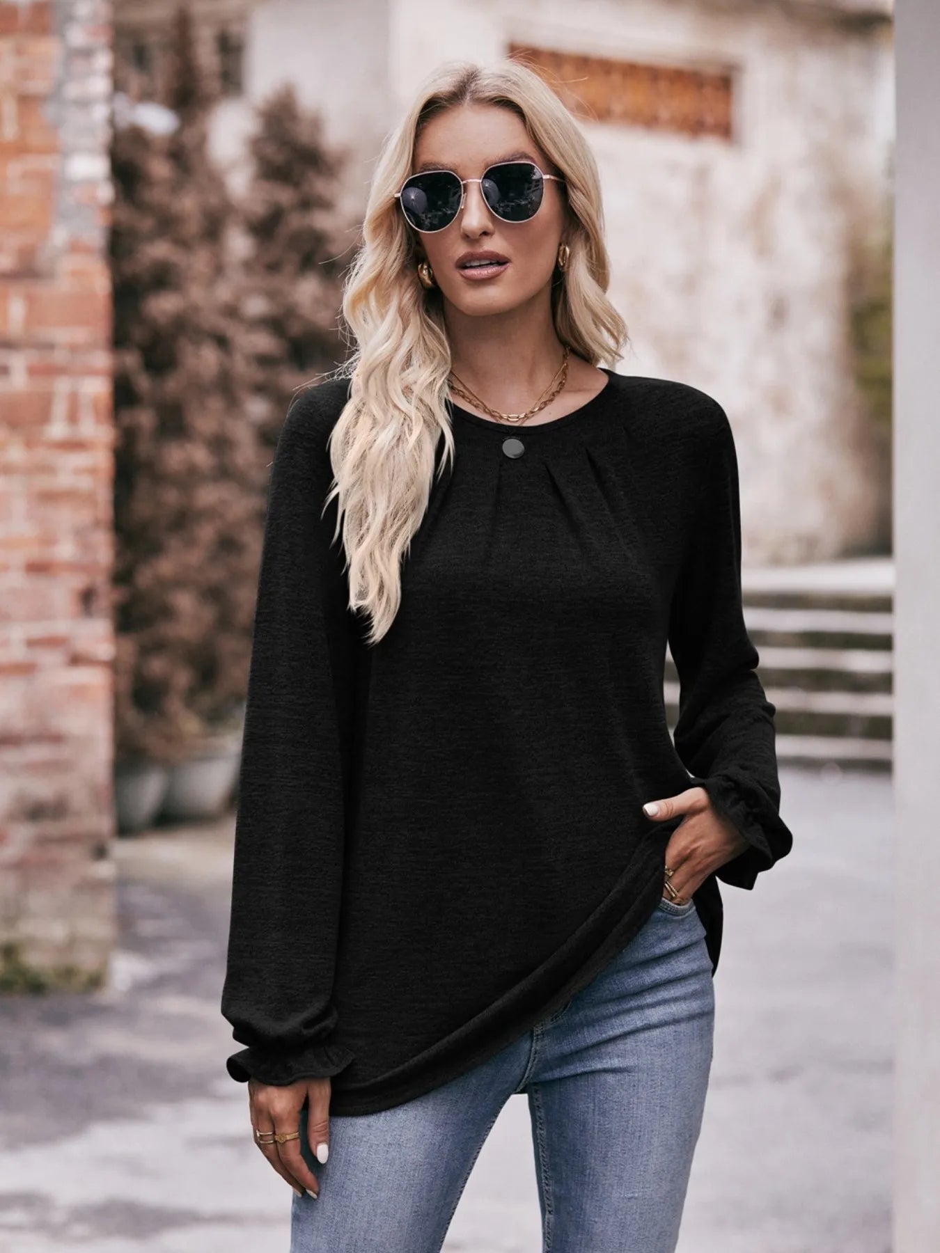 Woman wearing a black long-sleeve top and blue jeans outdoors.