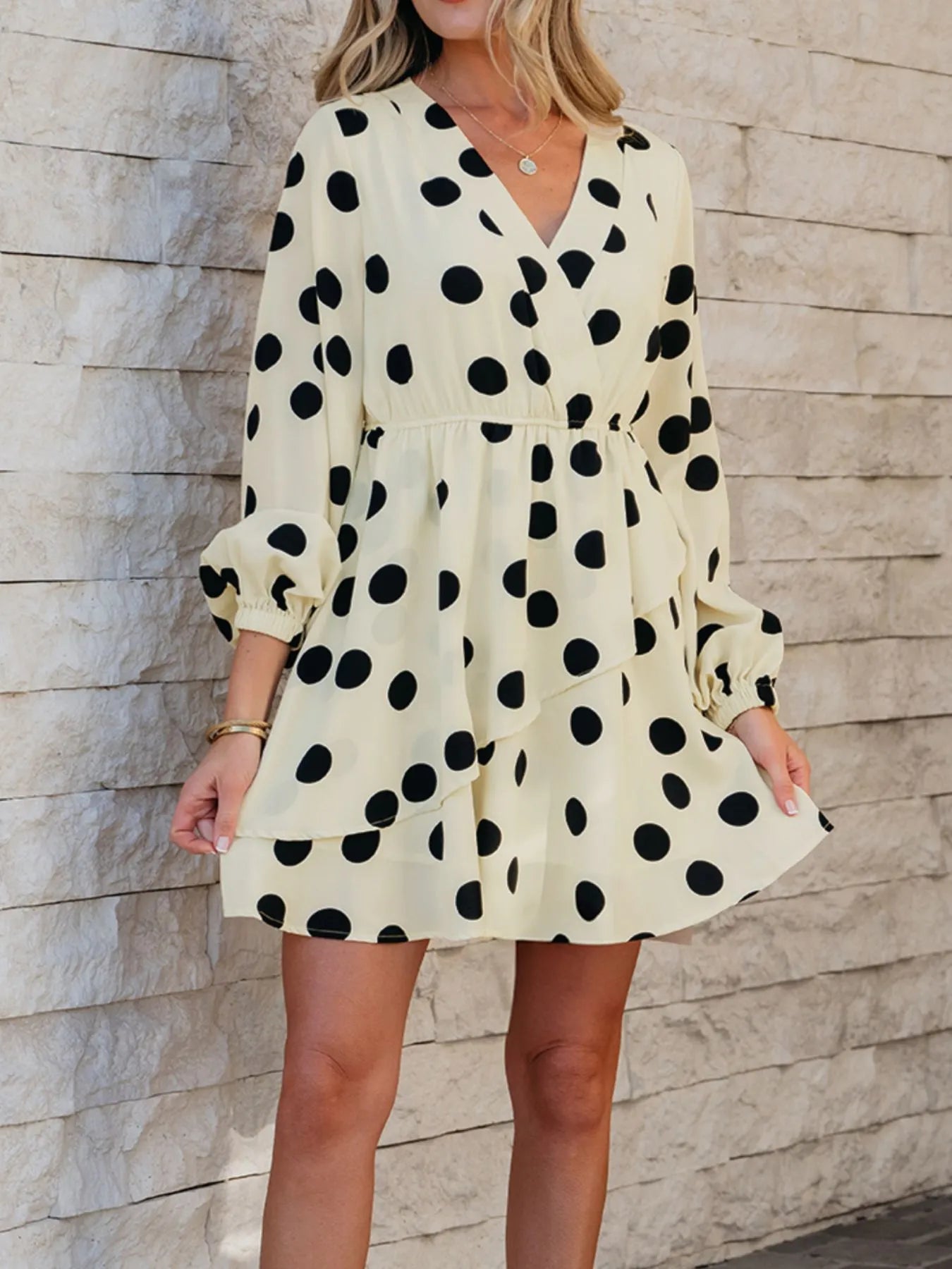 Woman wearing a polka dot dress against a stone wall.