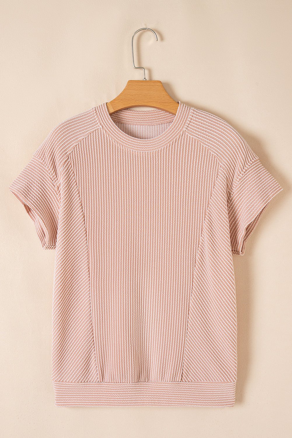Pink ribbed t-shirt on a wooden hanger against a beige background
