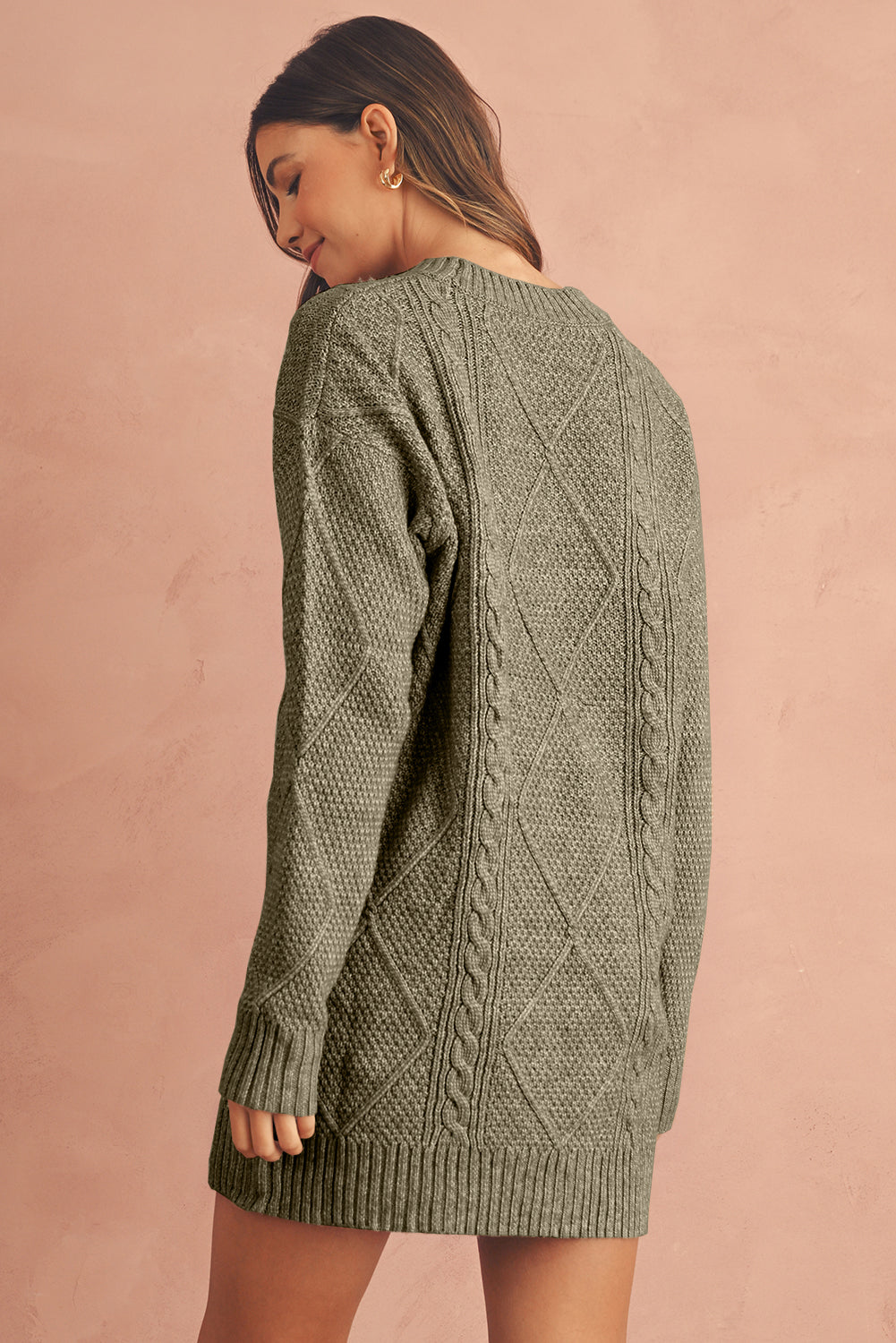 Woman wearing a green cable knit sweater against a pink background