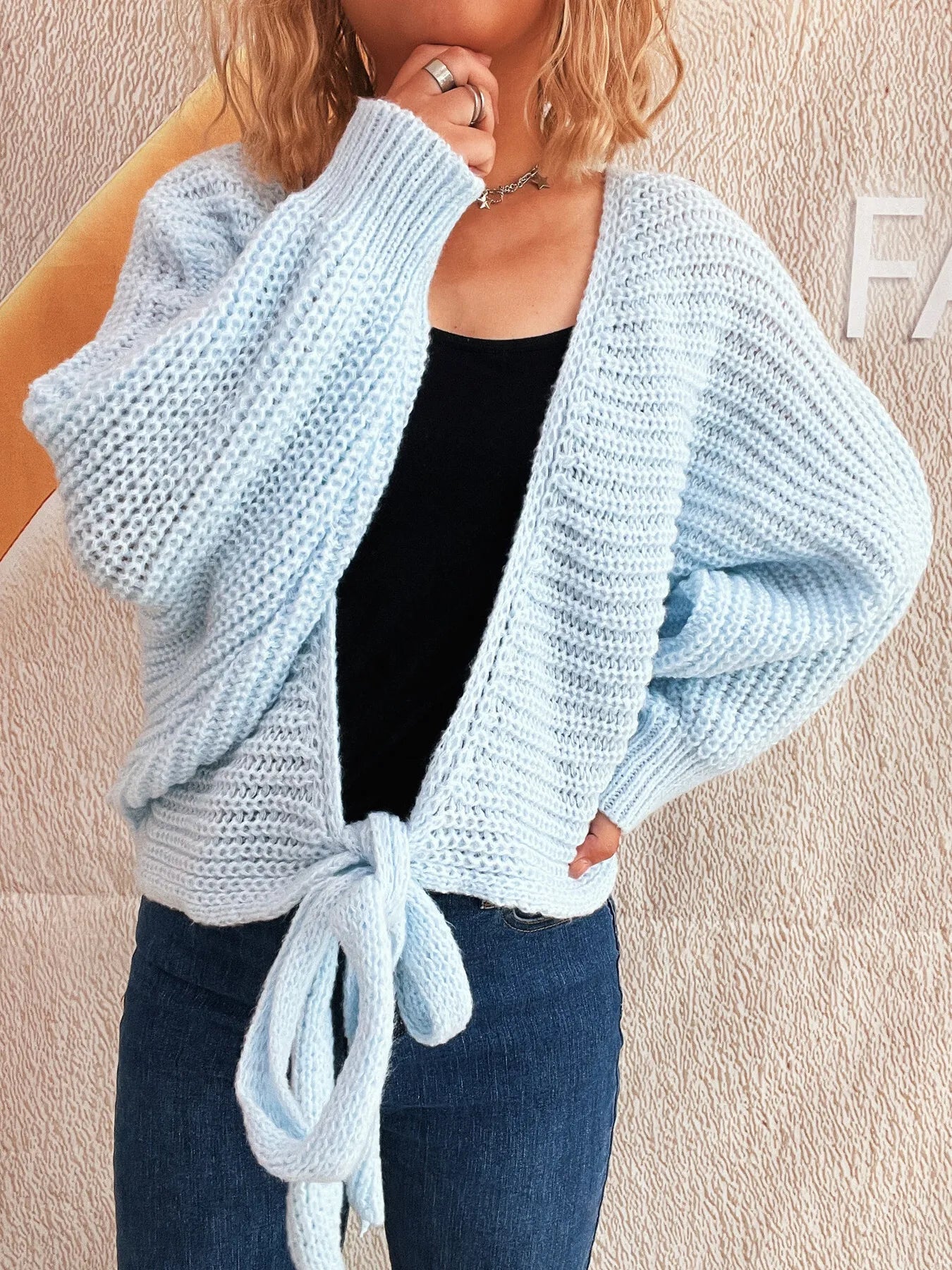 Light blue knitted cardigan worn by a person on a beige background