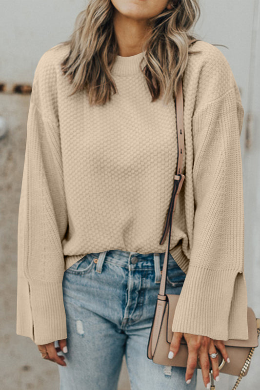 Person wearing a beige sweater and blue jeans with a neutral handbag.