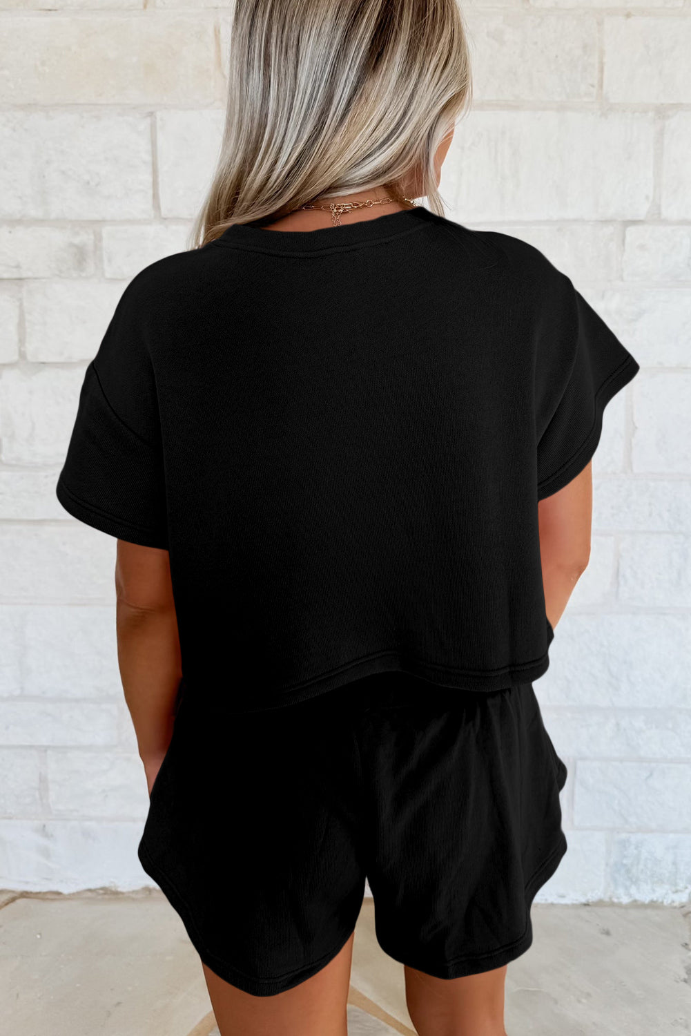 Person wearing a black outfit against a white brick wall.